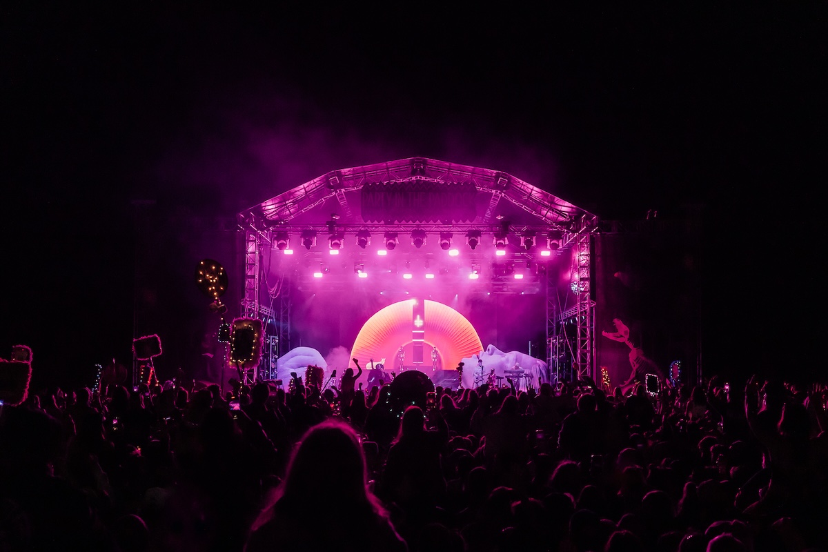 Nighttime crowd at Party in the Paddock festival watching a performance on a brightly lit pink stage.